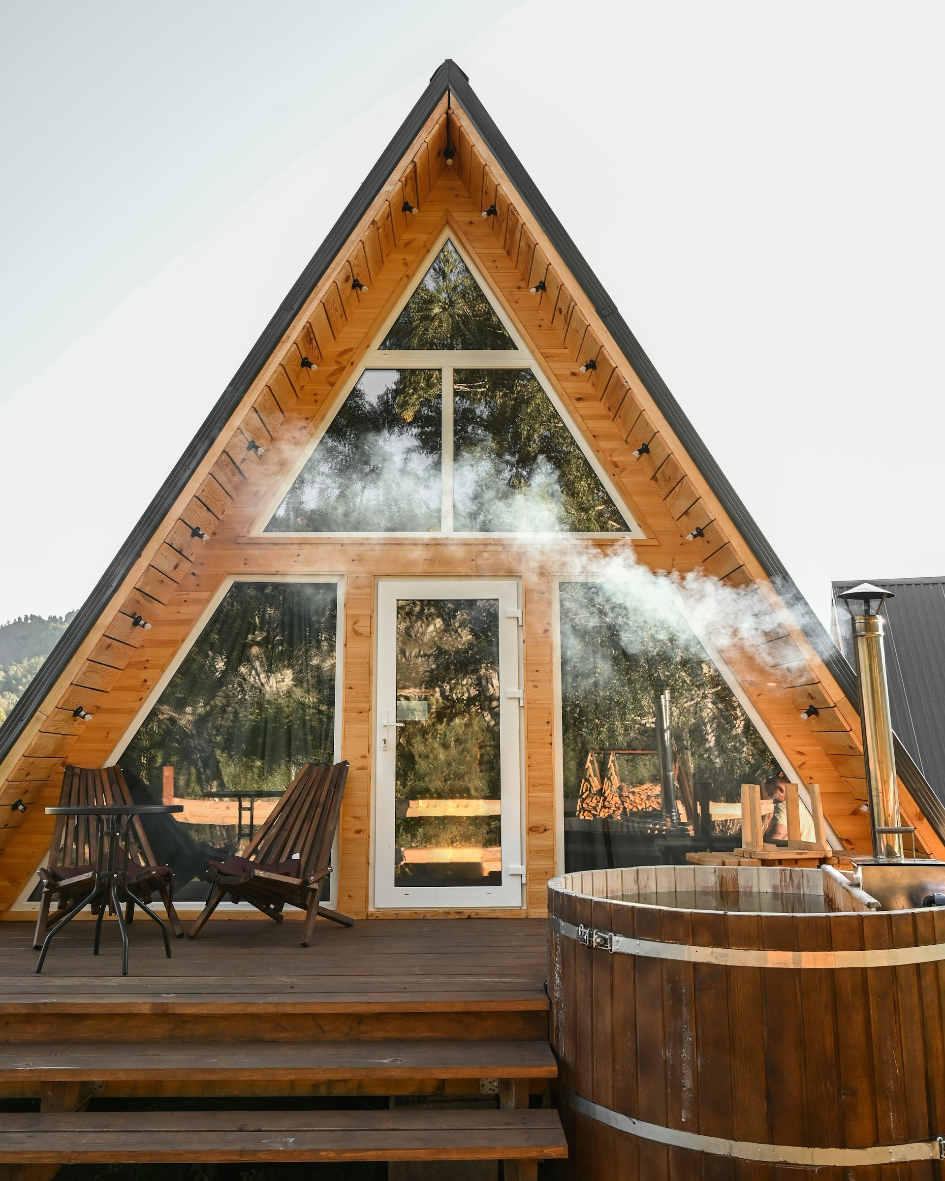 Cabana A‑frame văzută din pădure, la asfințit